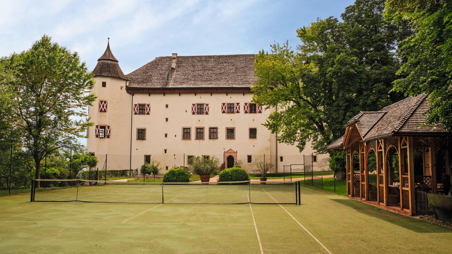 Pista de tenis vacía frente a un castillo antiguo con muchos ventanales.