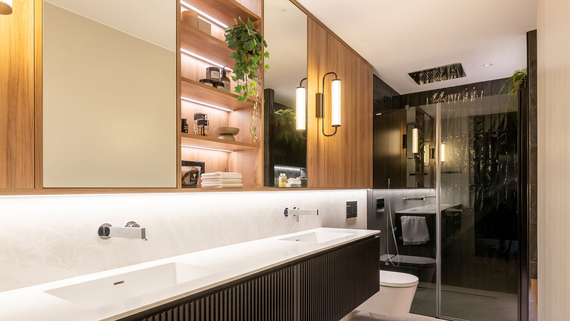 Baño con ducha, gran mueble bajolavabo de color negro, doble lavamanos, mueble de madera con armario, zona de baldas, espejo, aplique, iluminación interior 