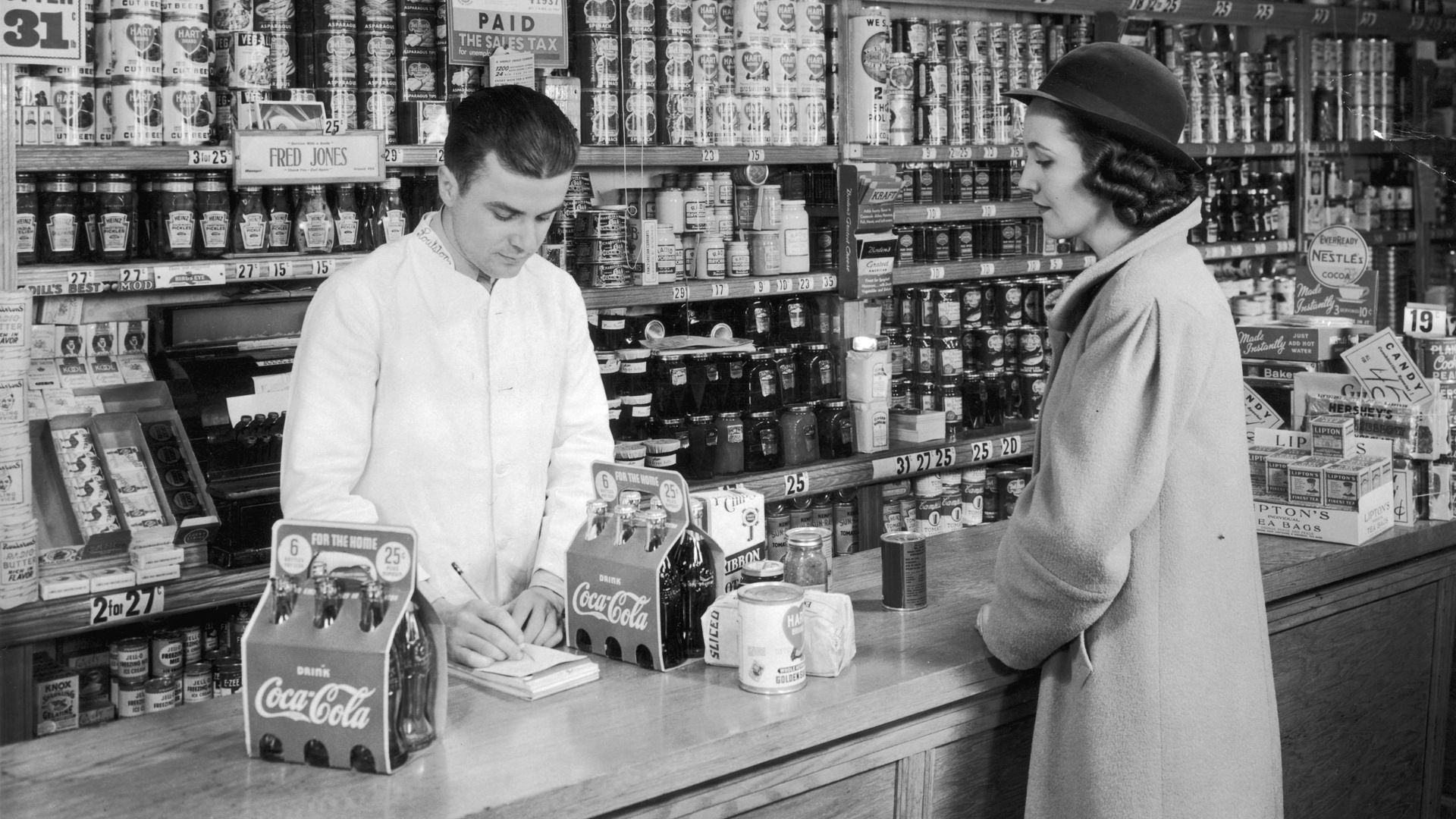 Una clienta compra varios packs de Coca-Cola en una tienda de alimentación de Estados Unidos hacia 1935, cuando la bebida ya comenzaba a convertirse en un fenómeno de consumo masivo