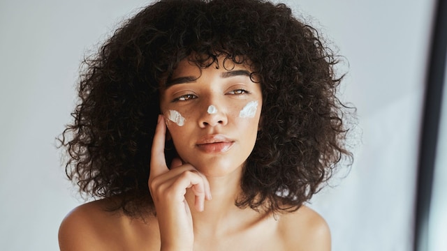 Chica con pelo rizado aplicándose una crema en la cara