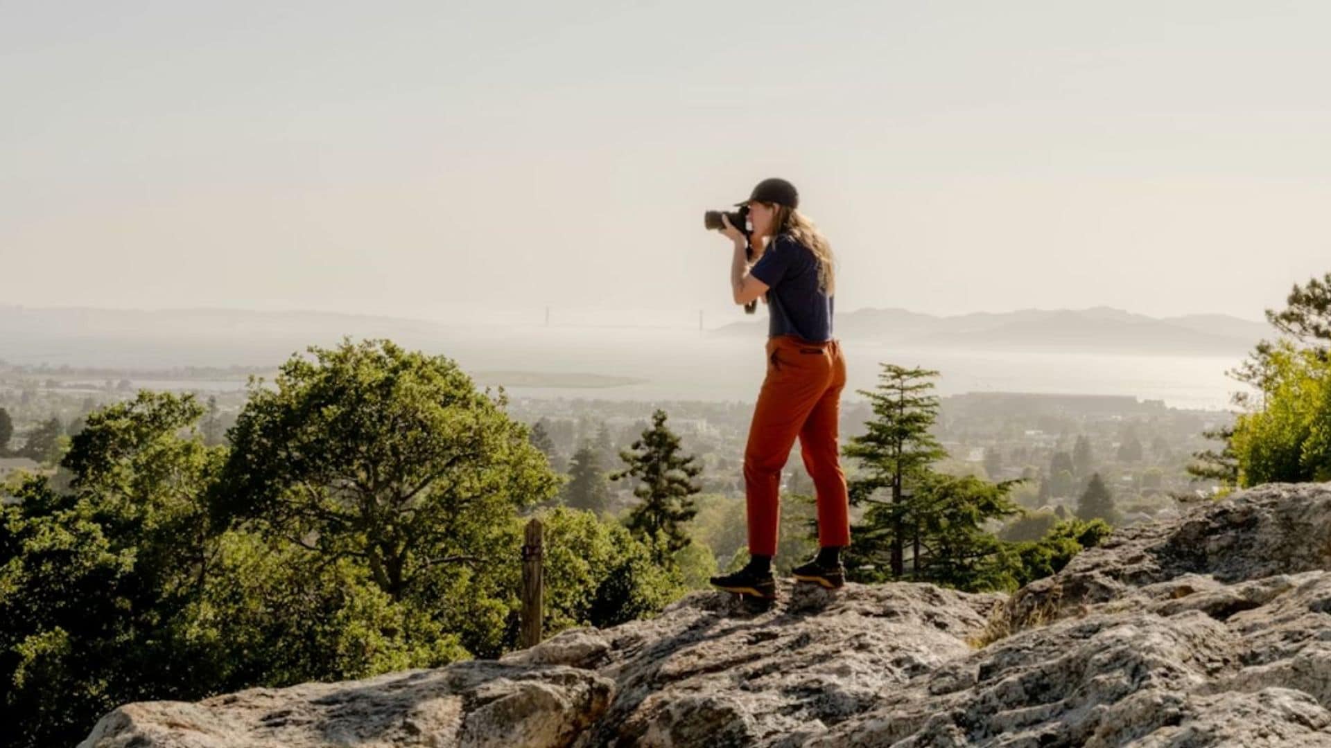 Mujer fotografiando con cámara profesional en lo alto de una montaña.