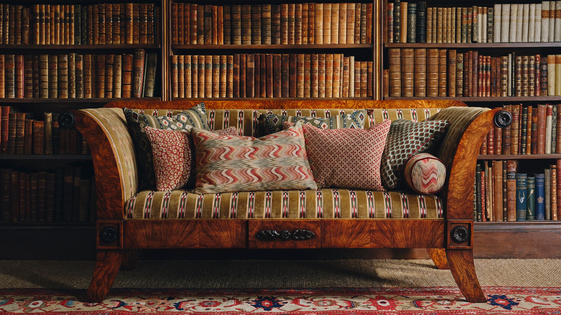 Salón con librería con libros, sofá de madera con tela estampada y cojines con distintos motivos