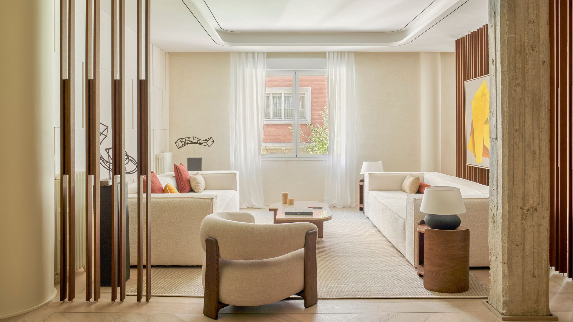 Salón en tonos neutros con sofás beige, butaca beige, columnas, cojines de colores, alfombra beige