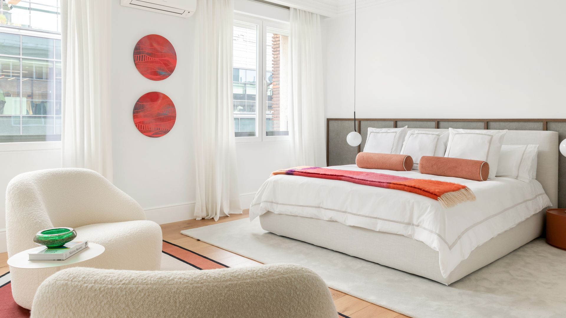 Dormitorio blanco con cabecero a medida, ropa de cama blanca, manta y adornos en rojo, cortinas blancas 