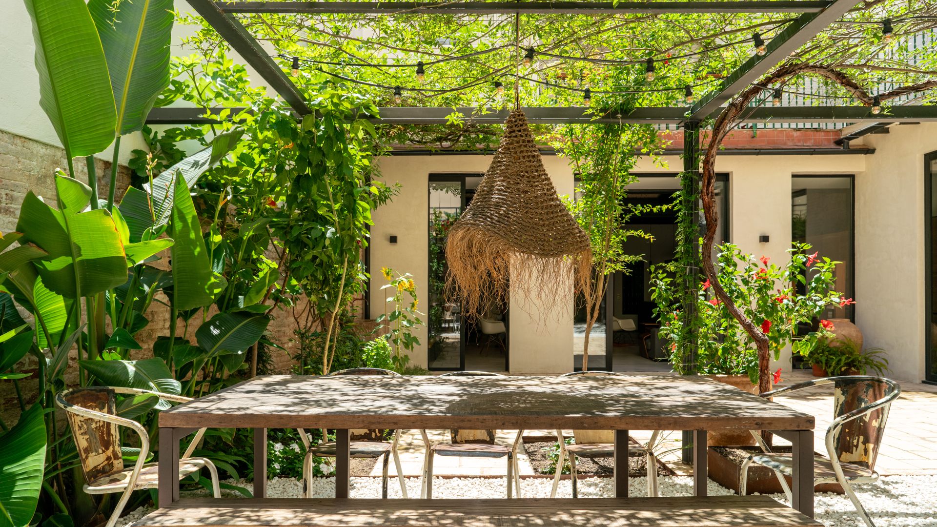 Patio con pérgola con plantas, mesa de comedor con banco, lámpara de techo de fibras vegetales