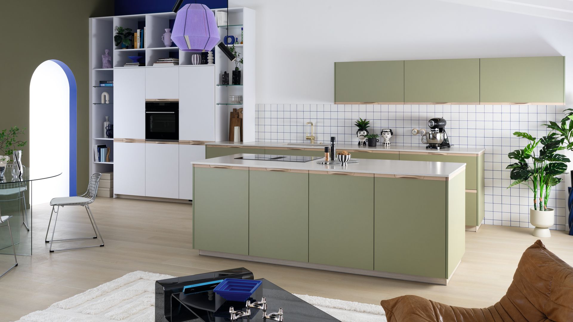 Cocina abierta al salón con muebles verdes, azulejos blancos y lámparas de techo moradas
