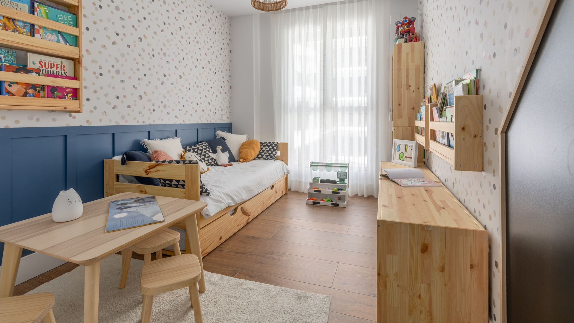 Habitación infantil con papel pintado, muebles de madera natural, estanterías, zócalo alto azul 