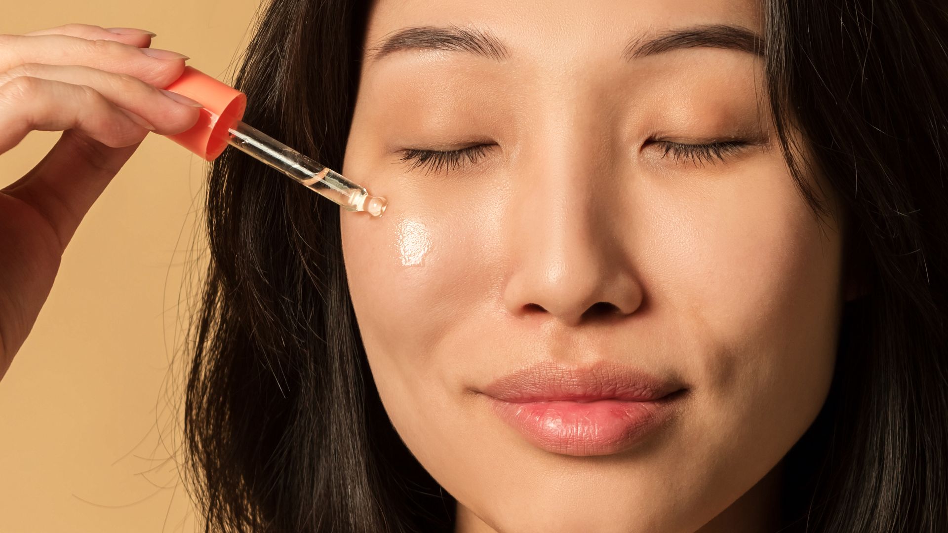 Rostro de mujer coreana con piel lisa mientras se aplica un sérum facial