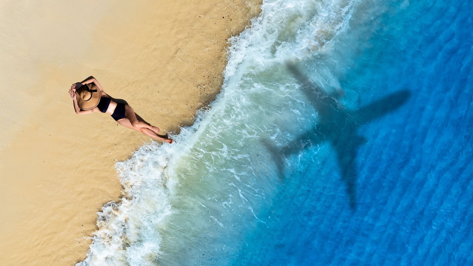 Mujer en una playa y sombra de un avión
