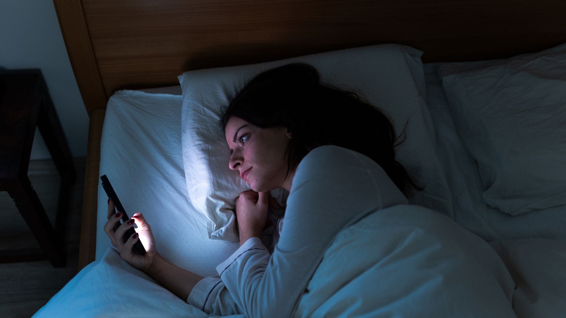 mujer mirando el móvil por la noche, mientras está en la cama