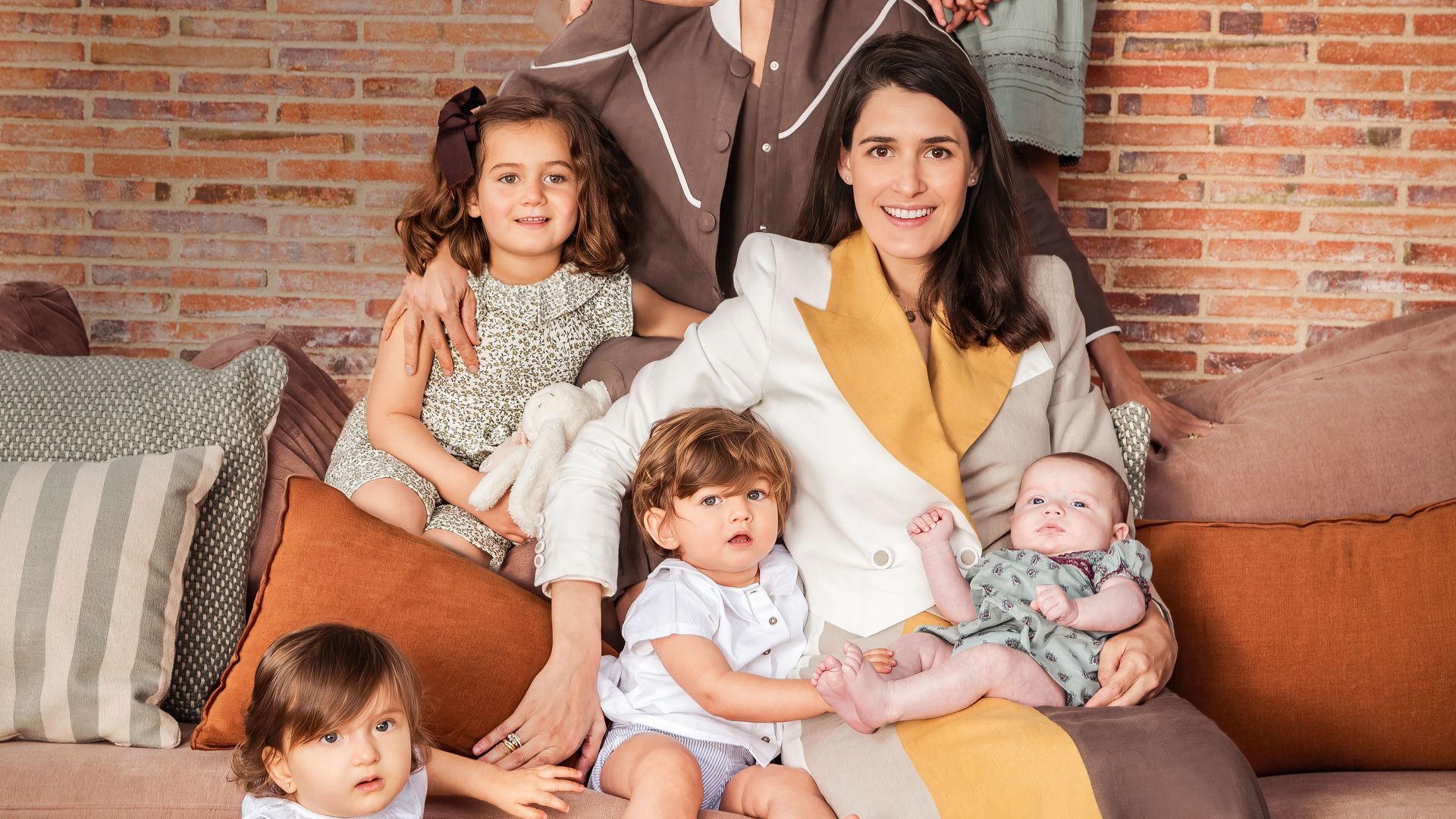  Las hermanas, con "looks" de su firma, con sus respectivos hijos, los cuatro de Inés y las dos niñas de Lucía: sentada sobre una maleta, la pequeña Lucía con "look" de Nícoli. En el sofá, Lucía madre abraza a Beltrán y a la pequeña Lola, ambos de Nícoli. Detrás, Inés rodeada por Casilda, con mono de flores de Coconut; Pelayo, con pantalón de Boboli y camisa de Nícoli, y, por último, Inés, con vestido de Nícoli y lazo en el pelo de Cóndor. Los peluches son de Pasito a Pasito