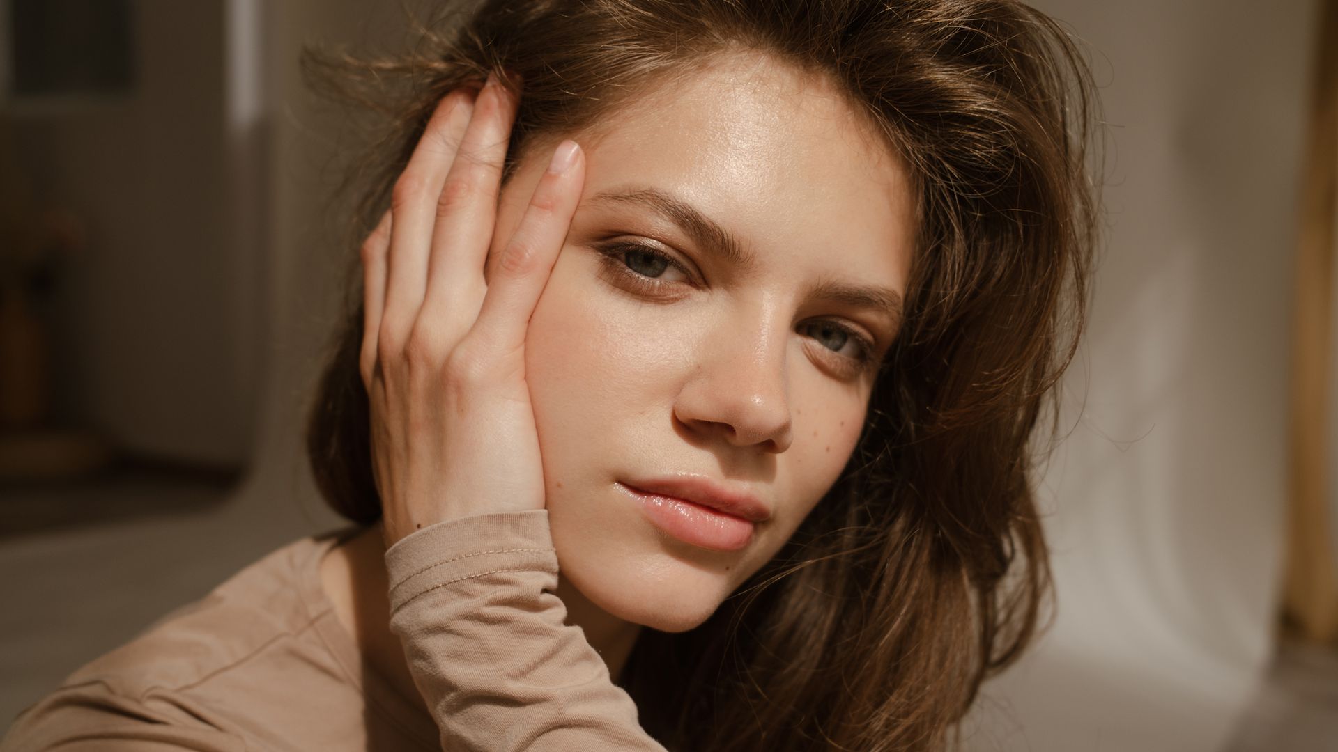 Rostro de mujer en primer plano con piel jugosa y cabello castaño ondulado y con volumen