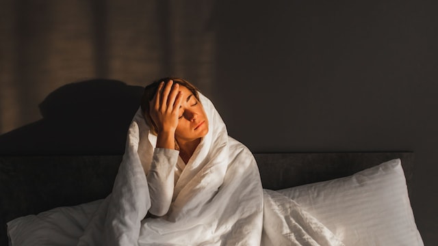 mujer se toca la cabeza en la cama, con molestia o dolor