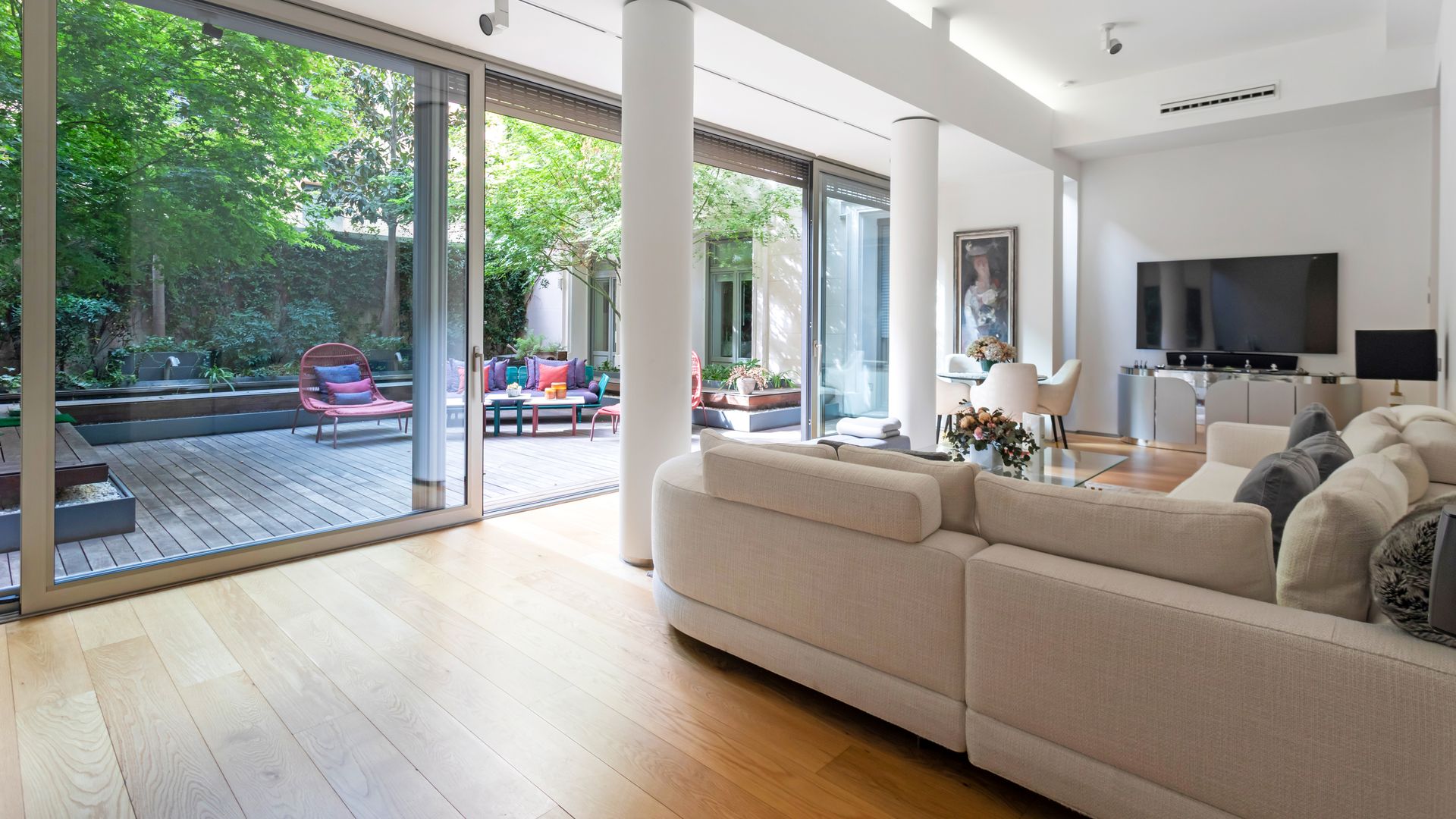 Salón con televisión, sofá blanco, columnas y grandes correderas que separan el salón de la terraza