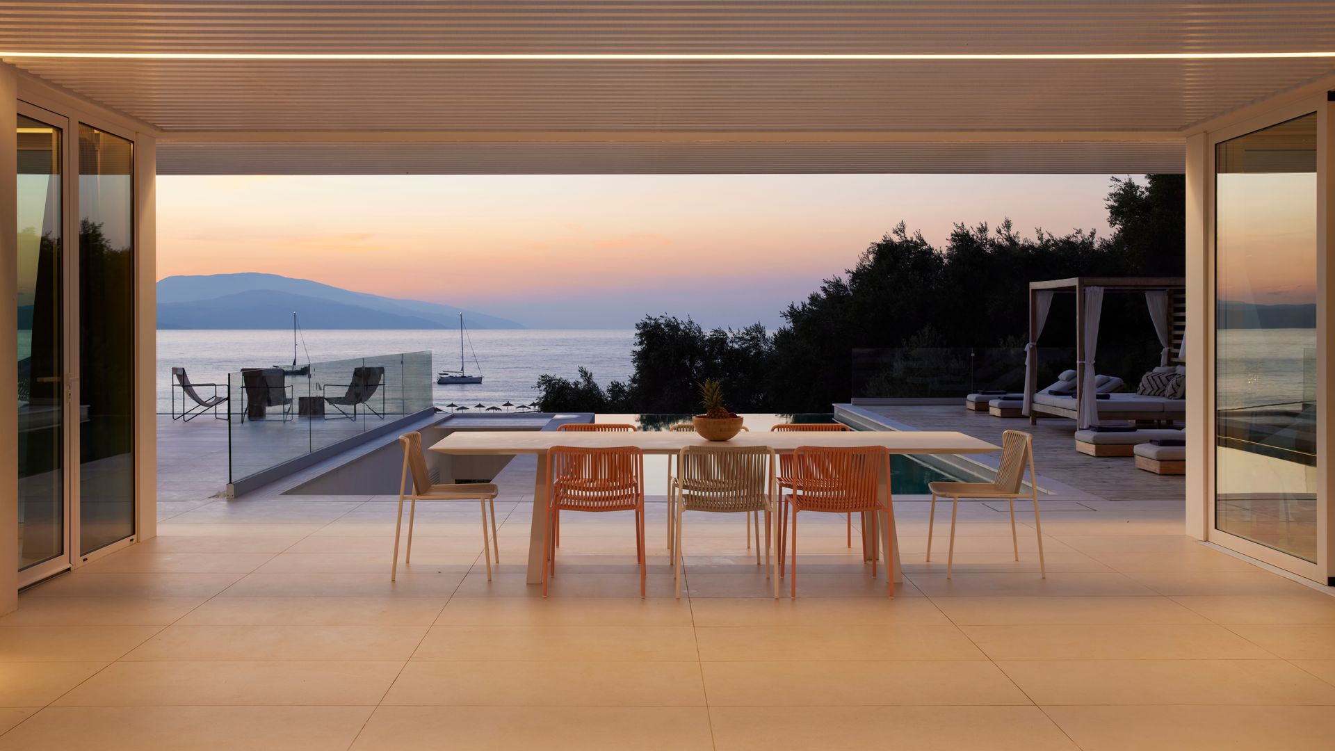 Comedor exterior con vistas al mar, bajo una pérgola con luz integrada, mesa de comedor y seis sillas 