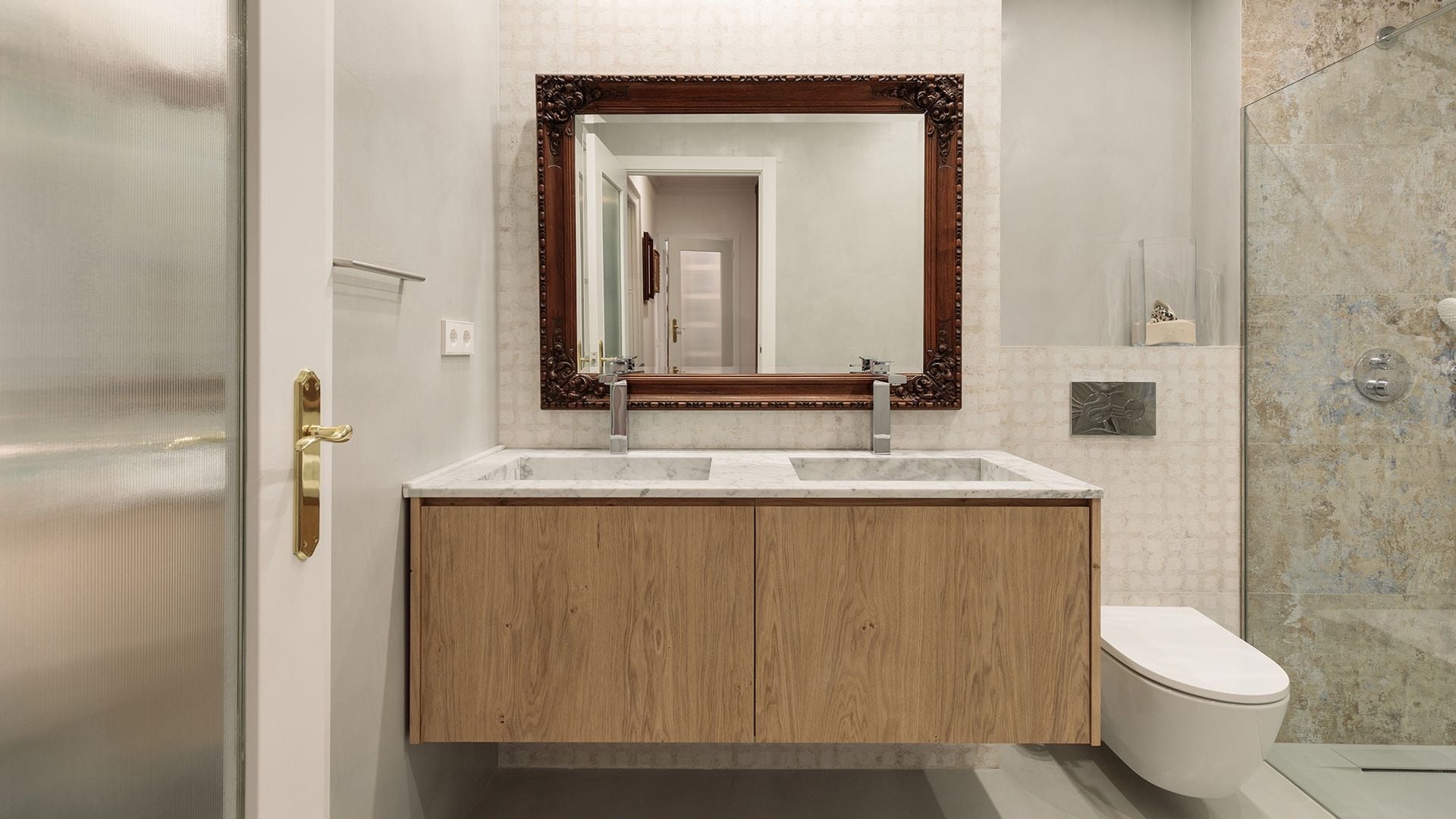 Baño con doble lavabo, espejo con el marco de madera, sanitario suspendido, ducha a ras de suelo con mampara, azulejos pared