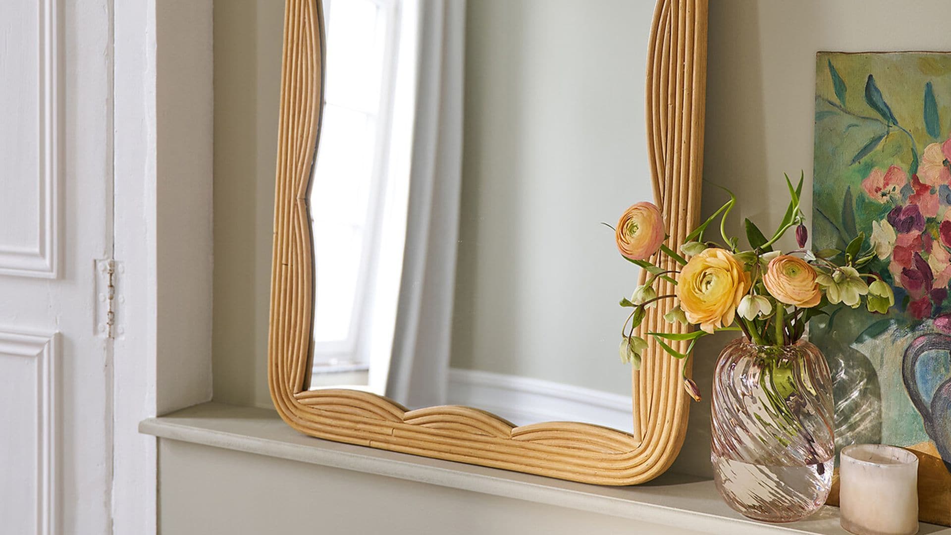 Repisa con espejo con marco de fibras vegetales, jarrón de cristal rosa con flores, vela y cuadro de jarrón con flores sin marco