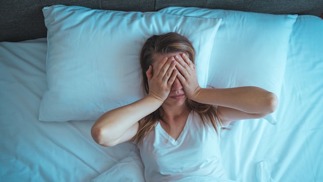 mujer sin poder dormir en la cama, tapándose los ojos con las manos