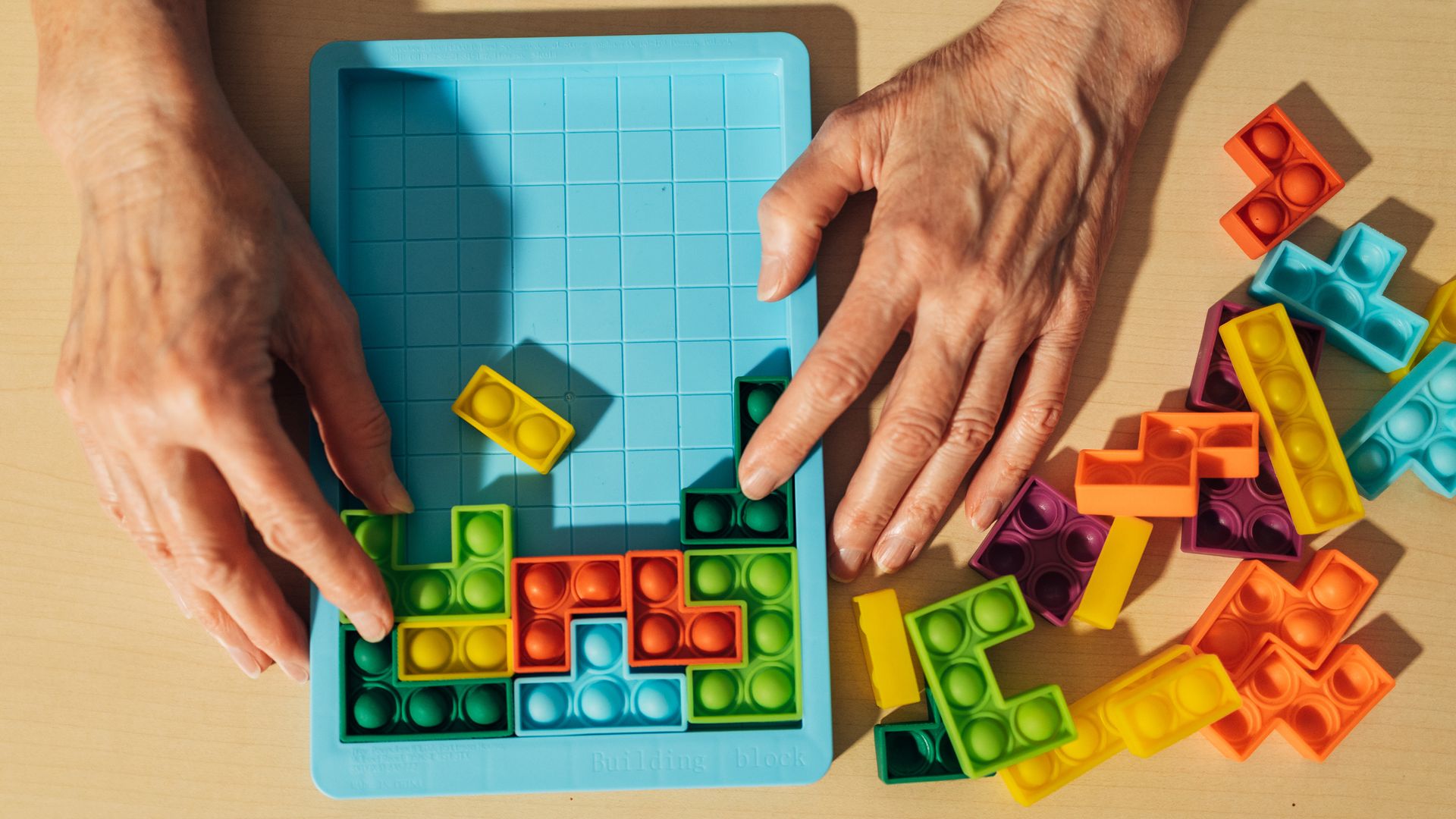 Persona mayor con un tetris de pop-it en la mano. Es un plano detalle de las manos y del juego sobre una mesa.
