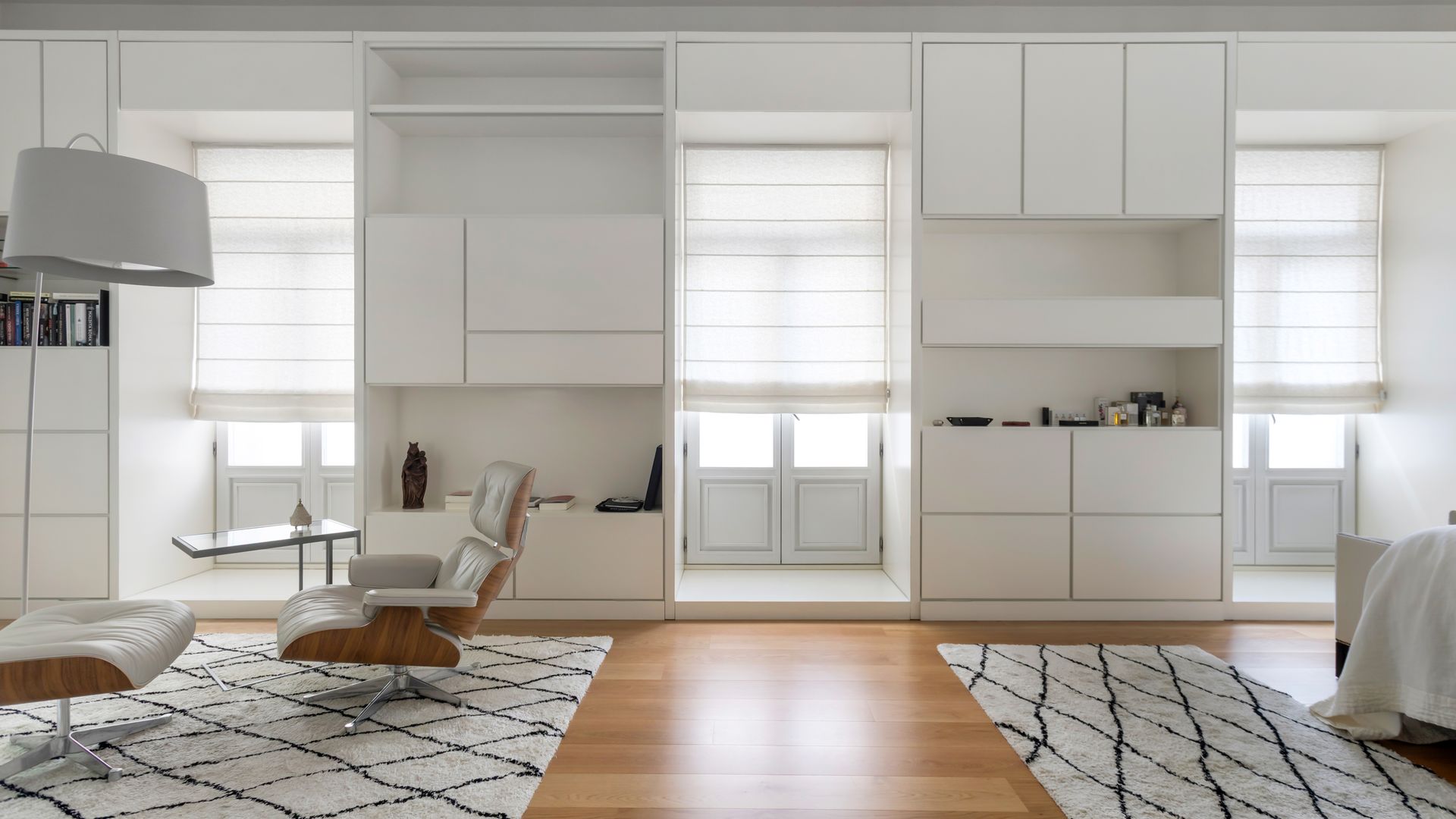 Dormitorio con tres balcones, estores en las ventanas de madera blancas, librerías a medida, alfombras de motivos geométricos 