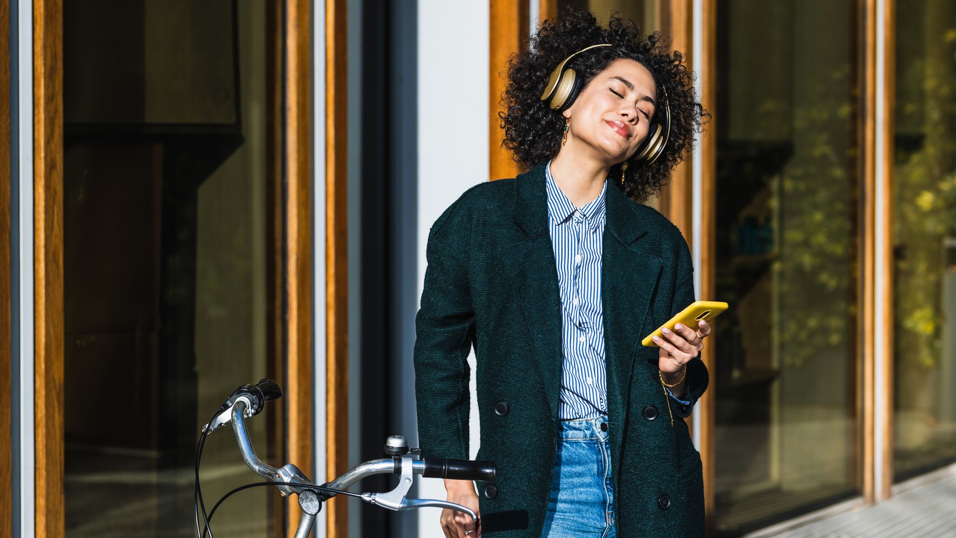 mujer escuchando música con auriculares junto a una bicicleta en la calle