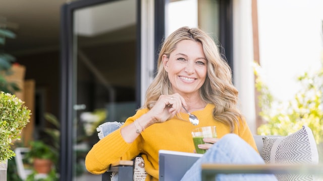 "Retrato de una mujer madura feliz sentada en la terraza con una tableta digital mientras disfruta de un batido verde."