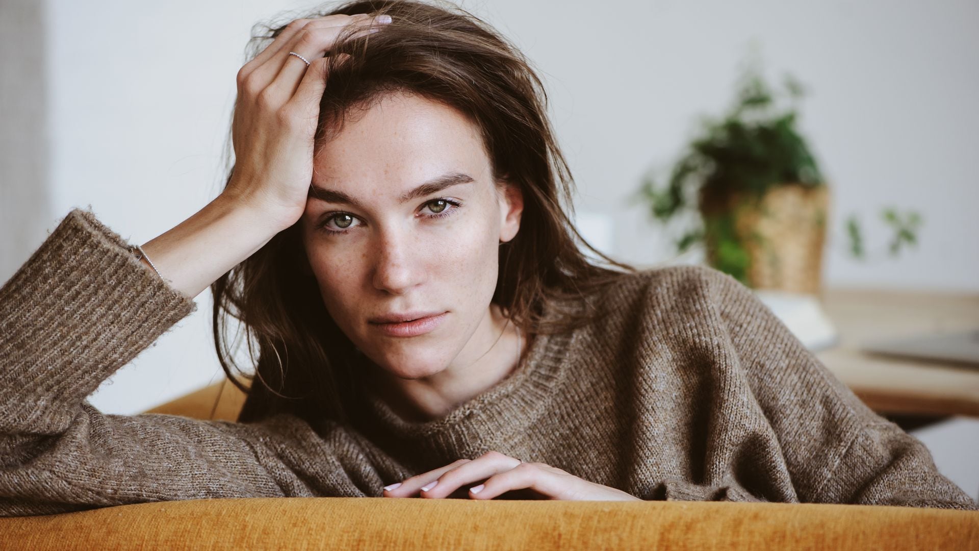 Mujer joven seria con la mano en la frente mirando a cámara 