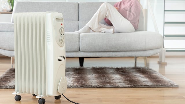 Una mujer descansando en un sofá con un calefactor delante