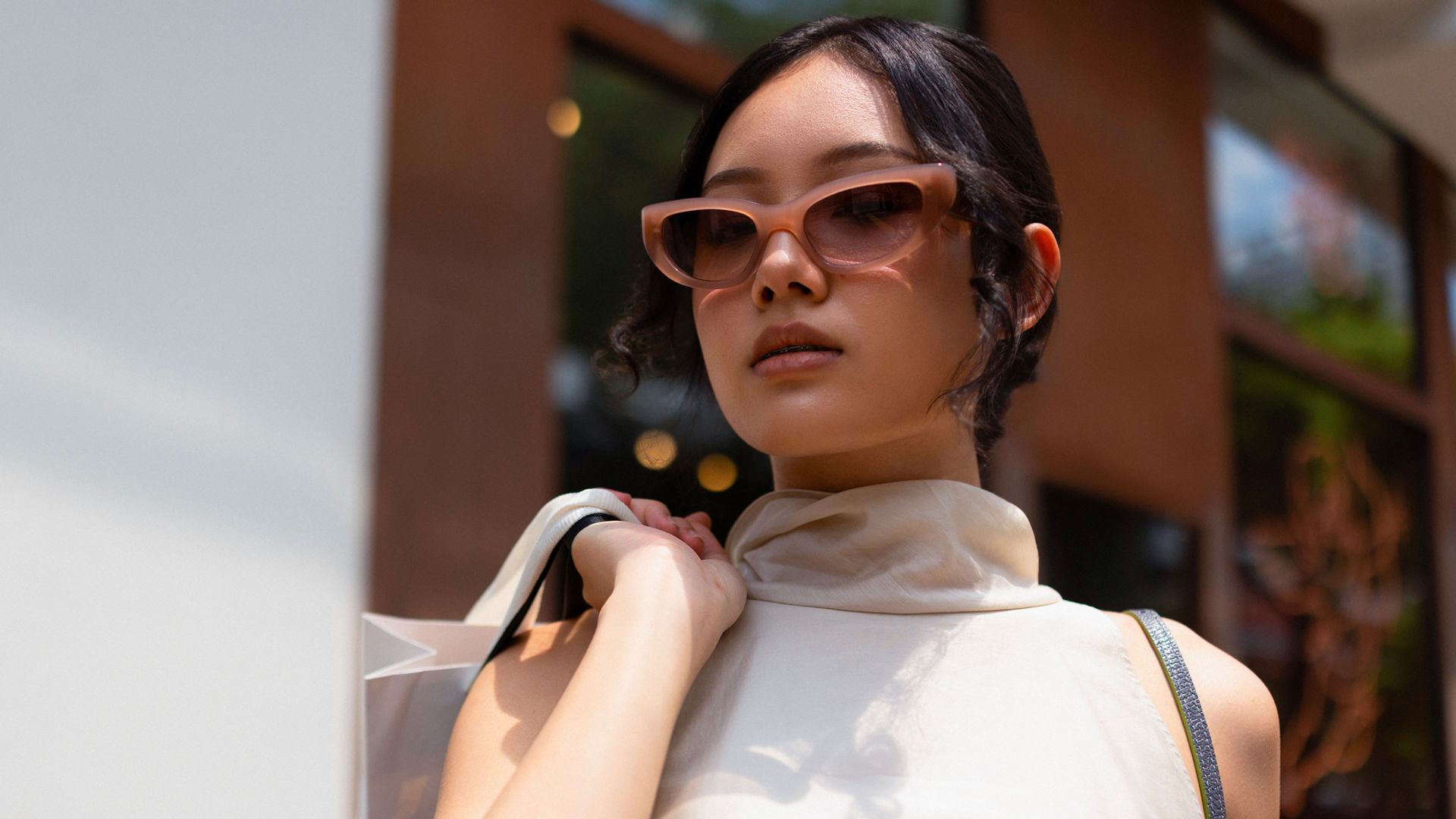 Mujer morena con gafas de sol y top con cuello vuelto satinado, con bolsas de compras