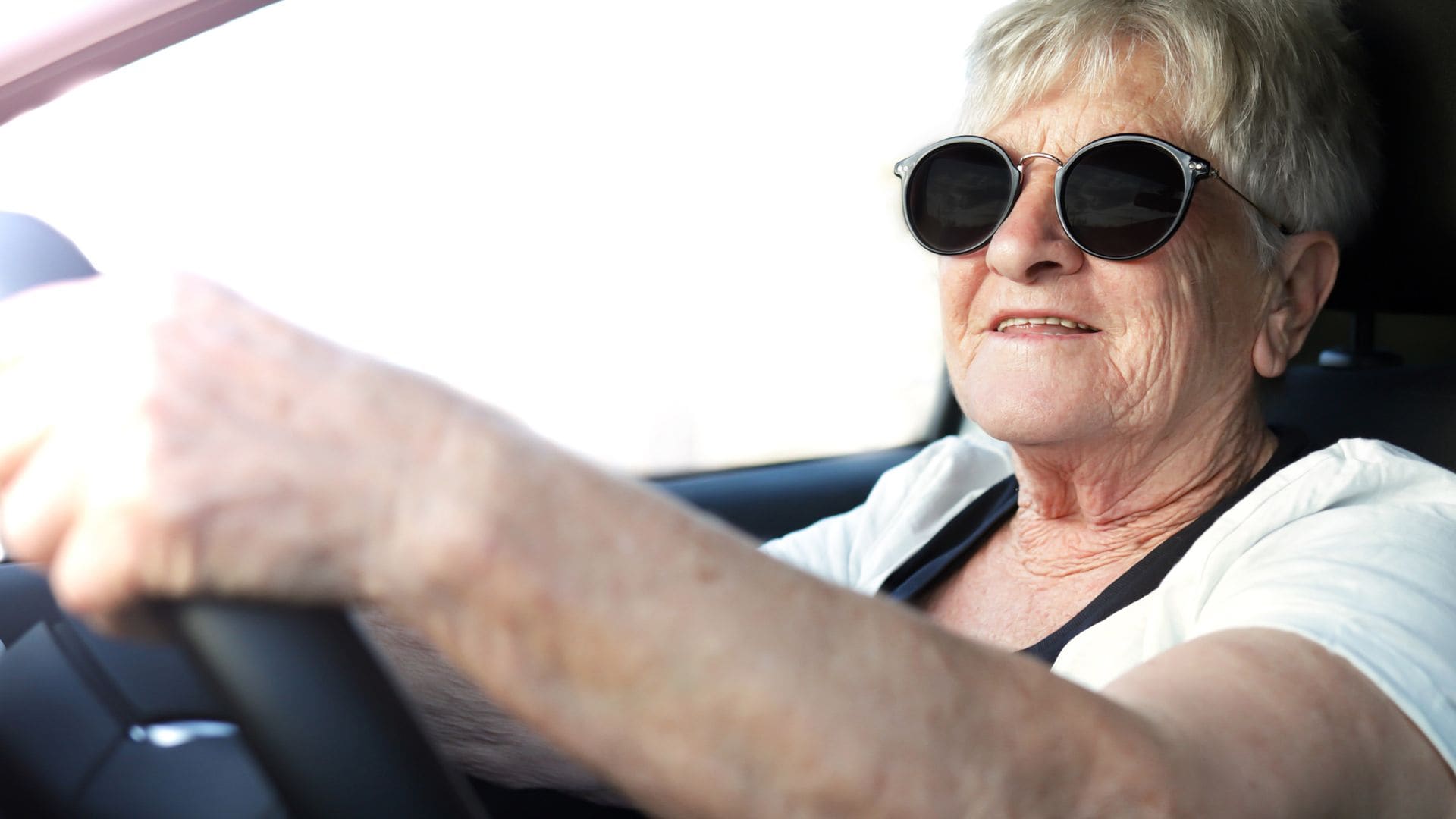 Una mujer mayor, sonriente y segura, disfruta al volante de su coche