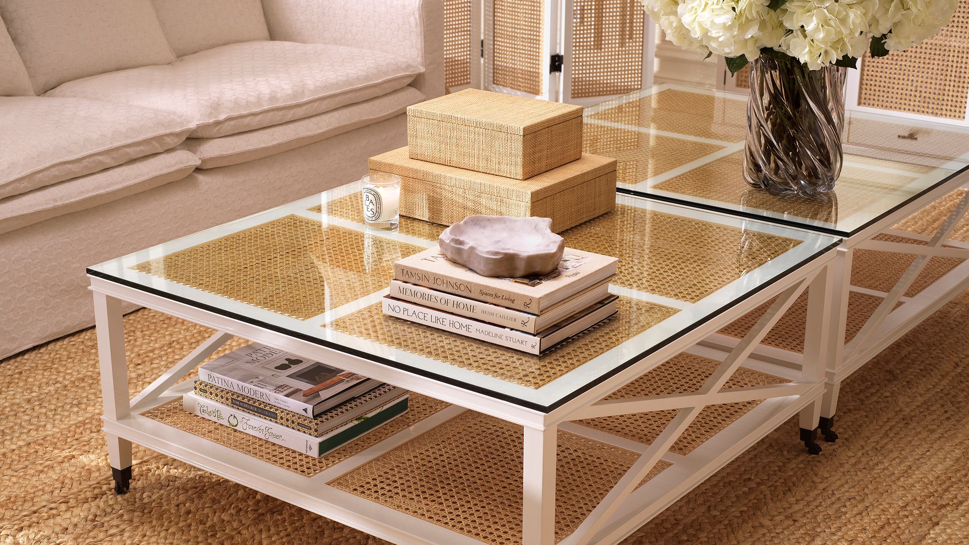 Salón con mesa de centro de rejilla y sobre de cristal con libros, jarrón con flores blancas, alfombra de fibras vegetales y sofá blanco