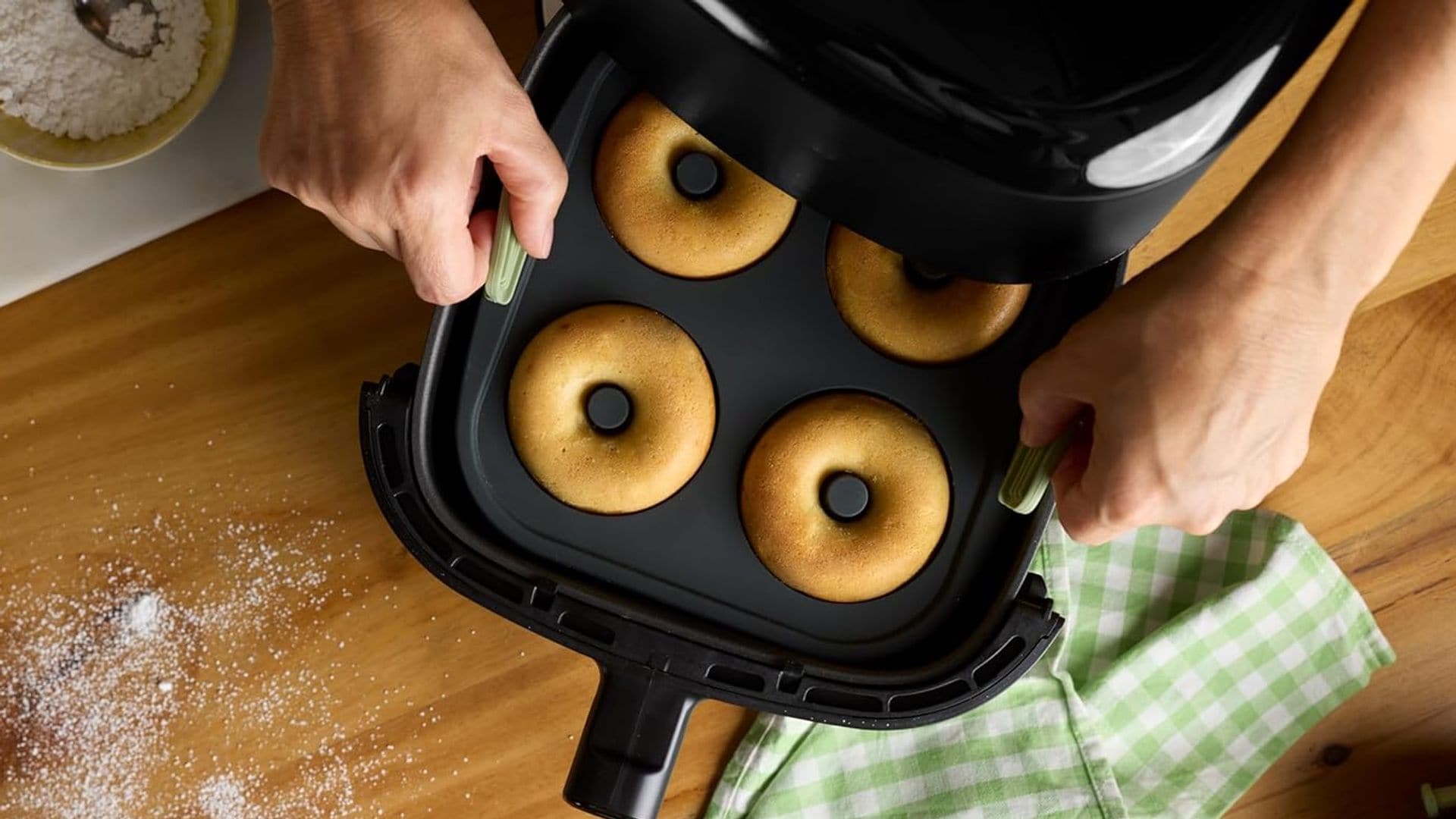 Manos de un hombre o mujer sacando en su molde unos dónuts caseros de la freidora de aire sobre la encimera.