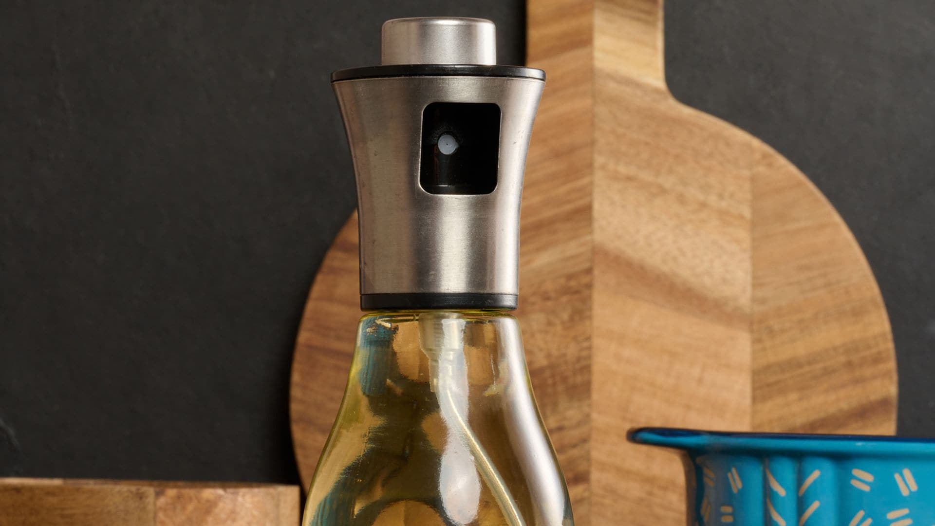Pulverizador de aceite de oliva en la cocina, sobre una encimera con otros utensilios de madera