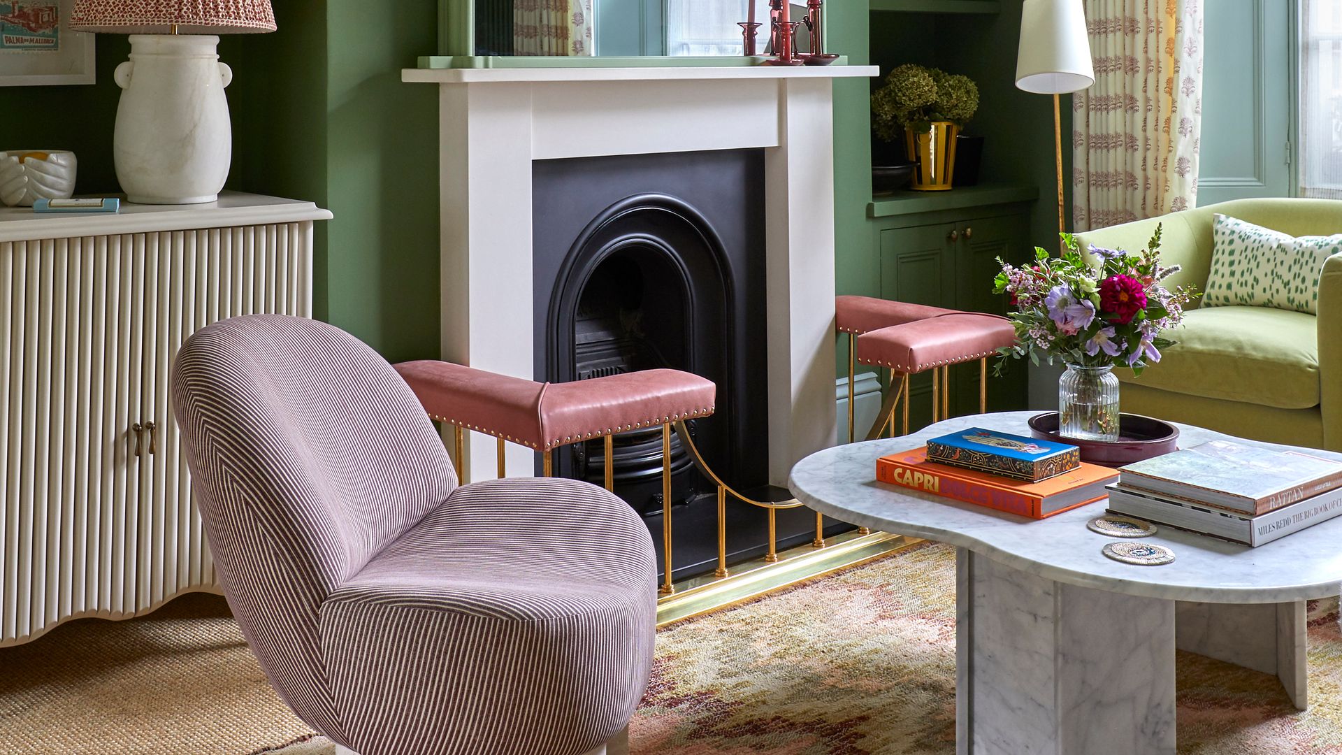 Salón con chimenea con las paredes verdes, estantería de obra del mismo. colore, butaca rosa, sillón verde, mesa de centro de mármol, espejo sobre la chimenea, alfombra 
