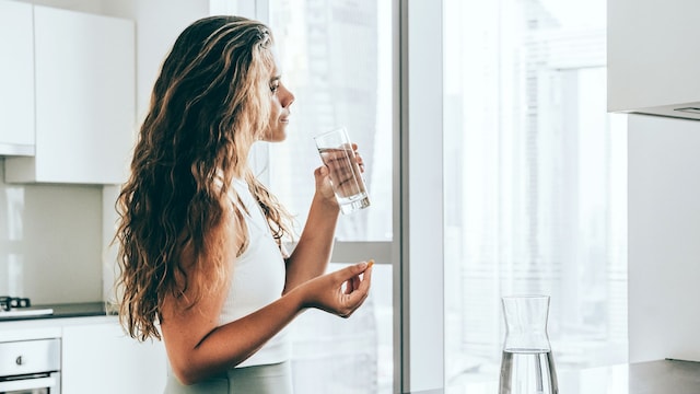 mujer joven tomando suplementos en la cocina