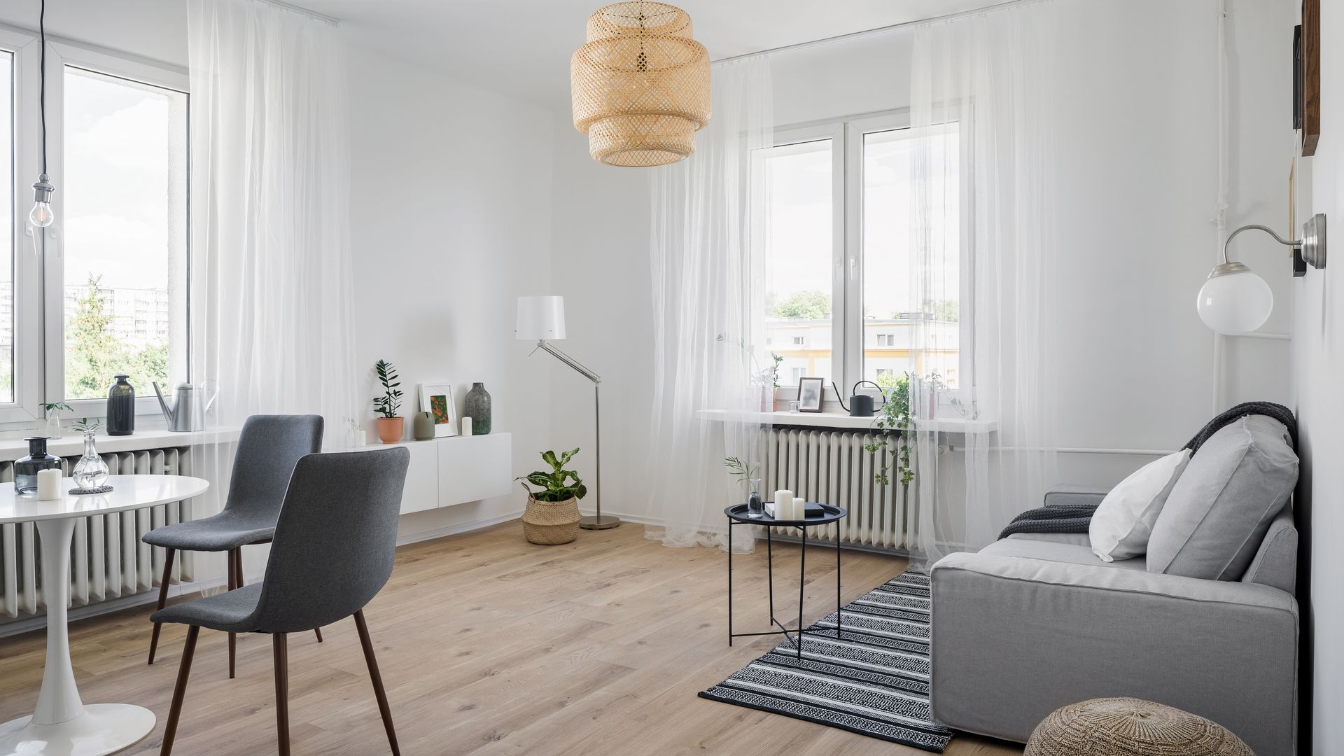 Salón comedor de estilo nórdico con suelo vinílico, sofá gris, mesa Tulip, sillas grises y lámpara de fibras naturales