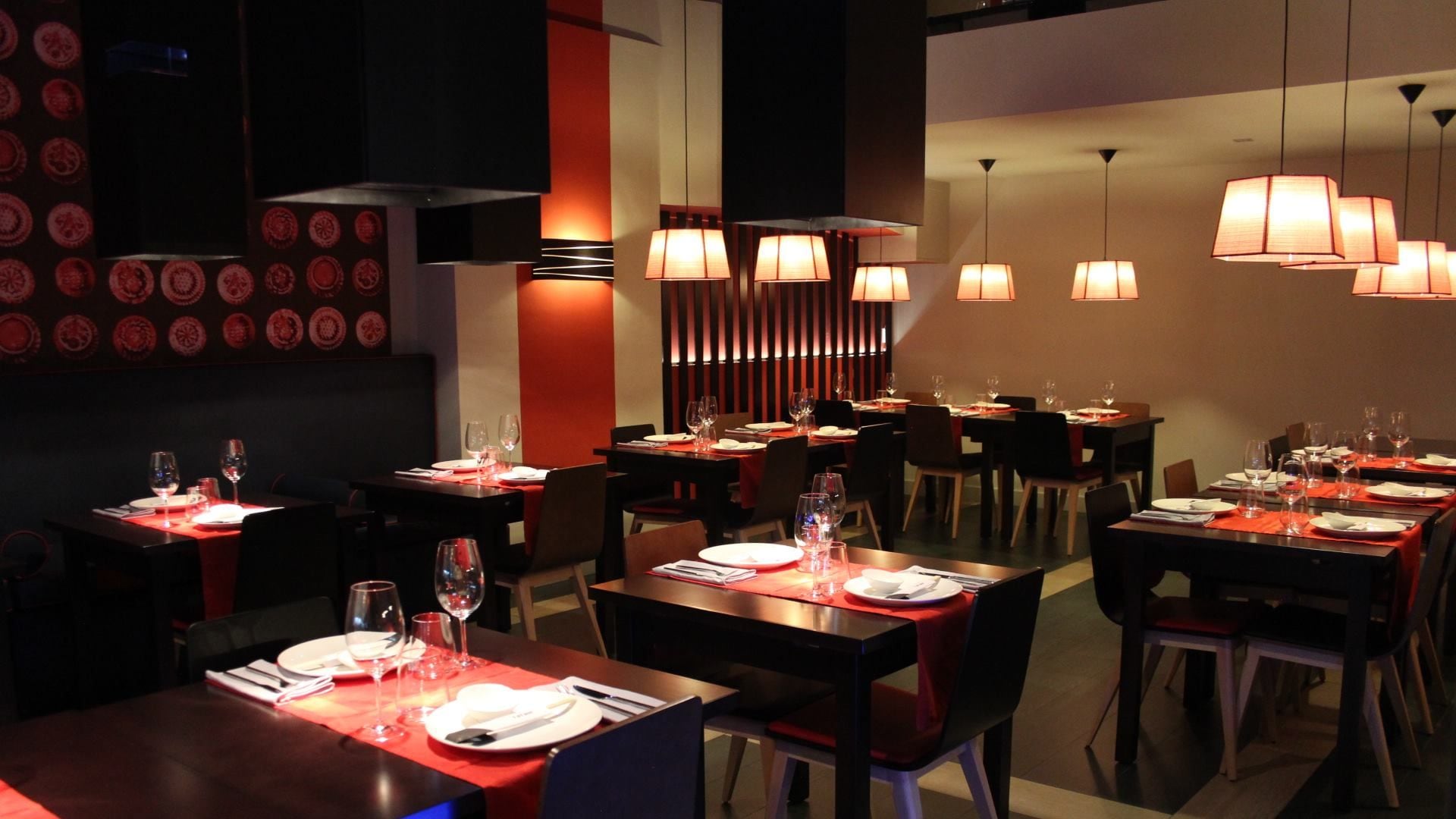 Restaurante con mesas de madera oscura, lámparas de techo, manteles rojos