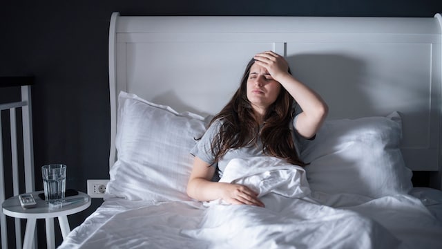 mujer se pone la mano en la cabeza mientras está en la cama