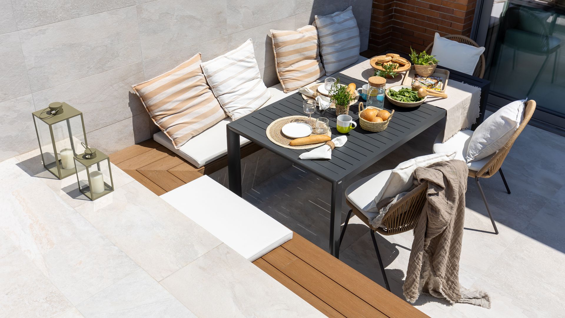 Terraza con banco de obra con cojines y mesa negra con platos y fuentes