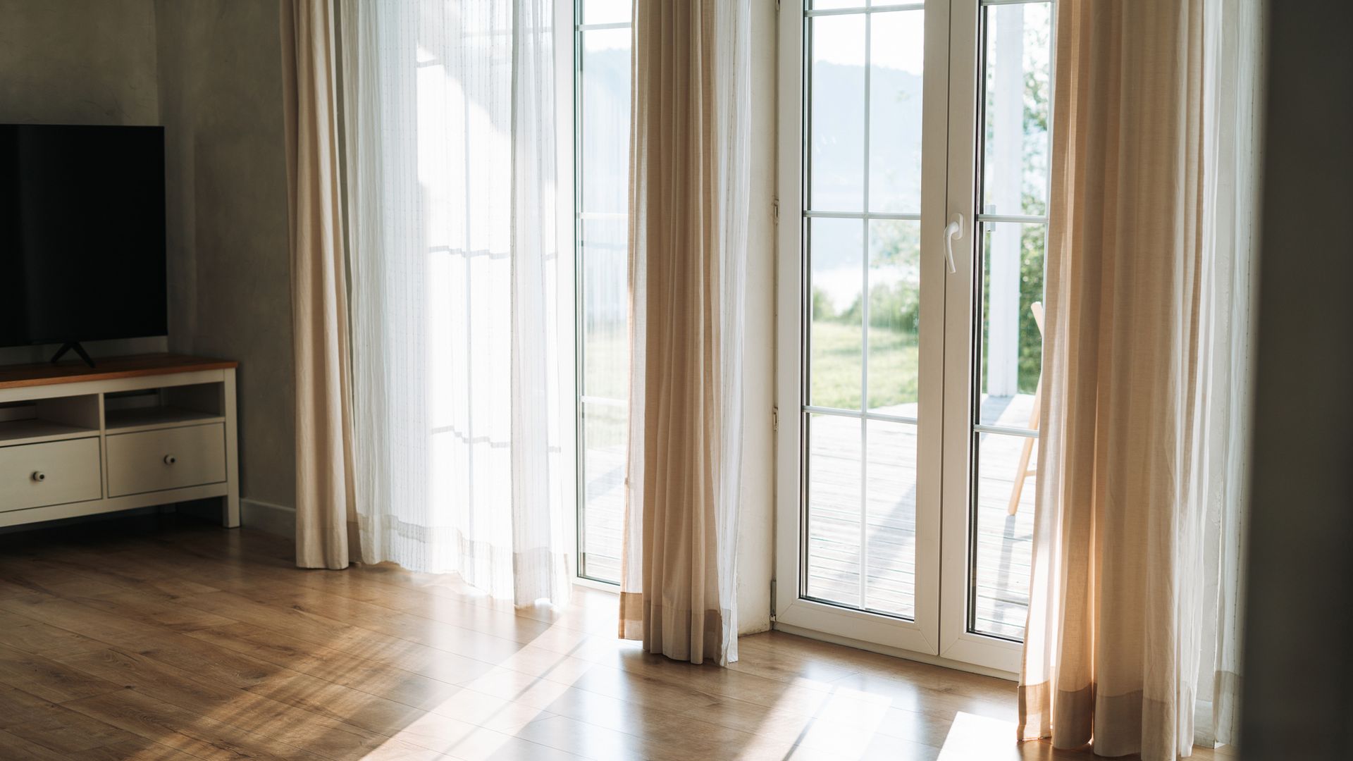 Ventanas de un salón con la entrada del sol en verano, en tonos beiges y blancos.