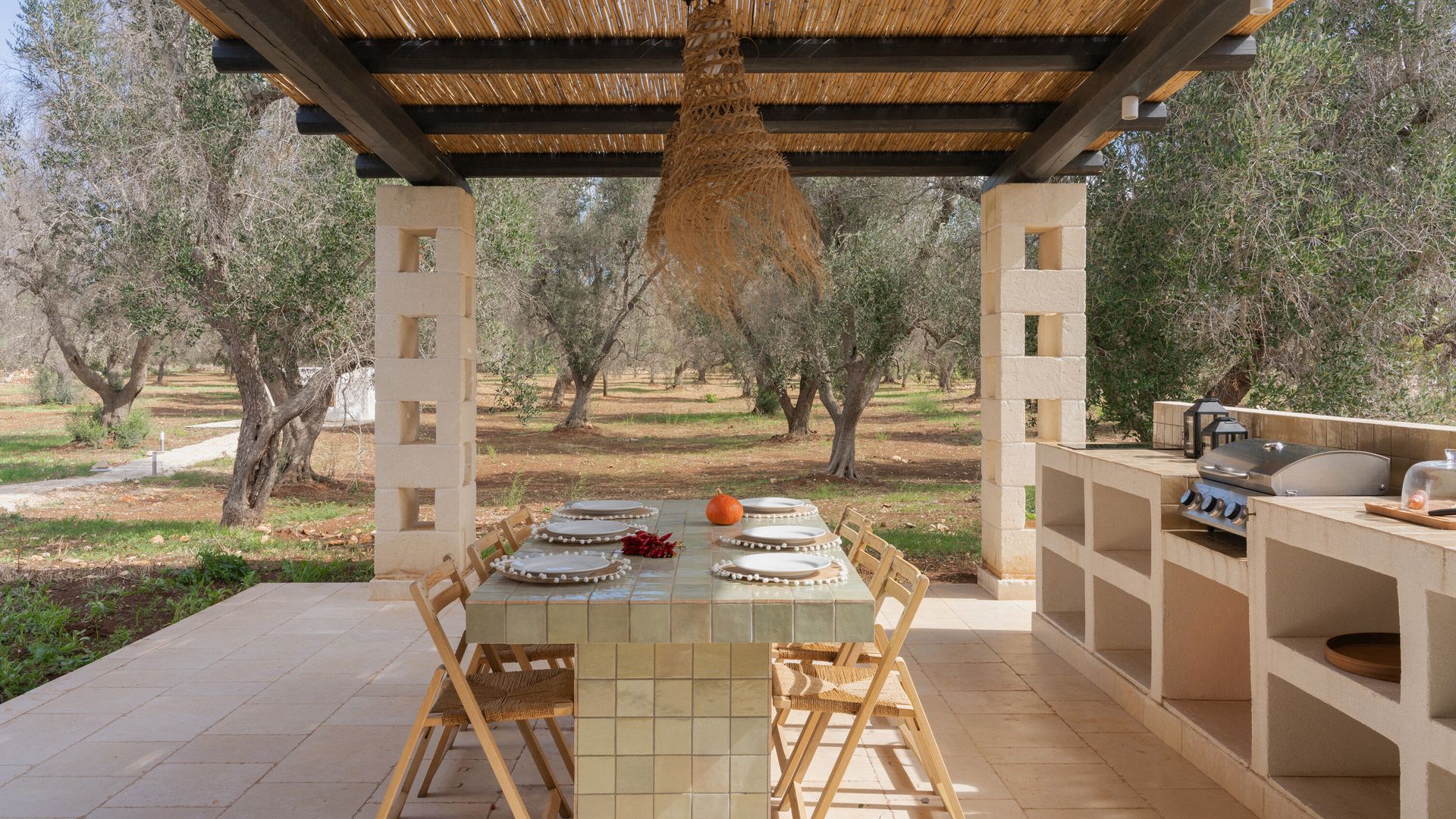 Cocina exterior bajo pérgola de caña, mesa de comedor de azulejos, silla de madera, cocina de obra 