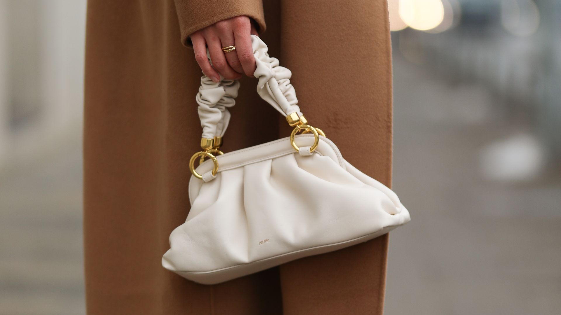 Louisa Theresa con pantalón de punto beis, zapatillas, abrigo cámel y bolso de mano blanco