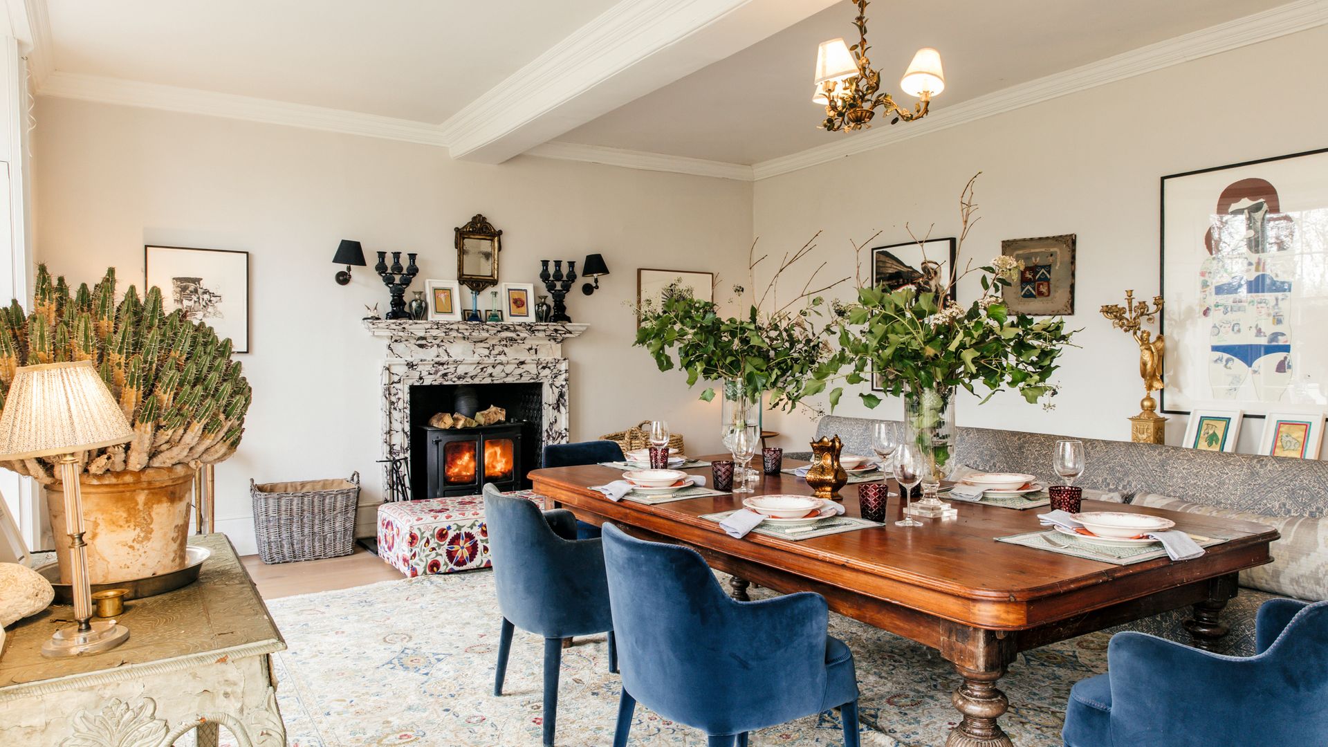 Comedor elegante con mesa de madera, sillas azules, chimenea y arreglos florales.