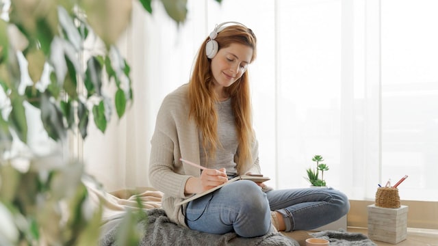 Mujer joven pelirroja escribiendo en un cuaderno en un salón con plantas