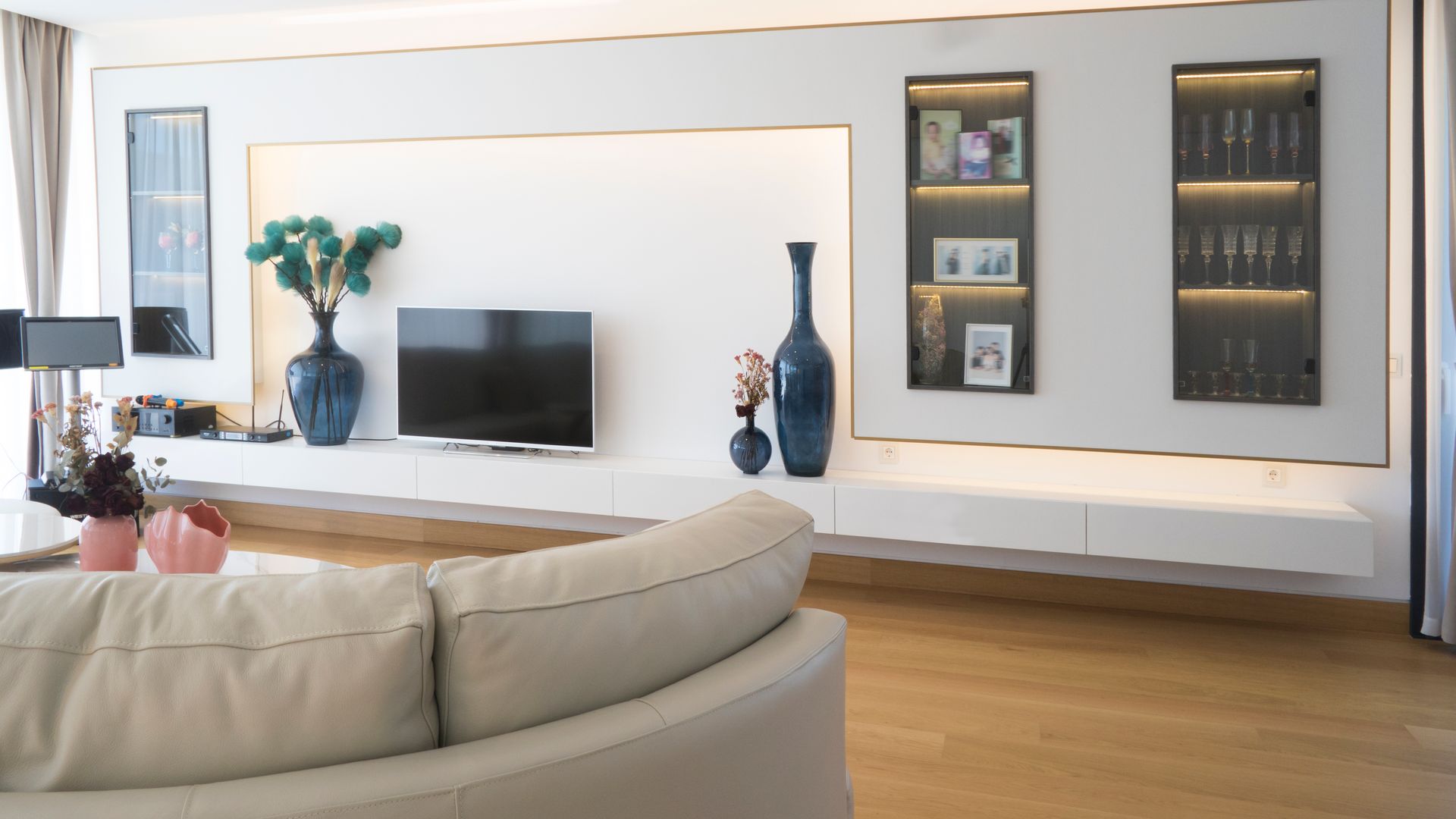Salón con sofá blanco, mueble a medida, vitrinas, suelo de madera, televisión