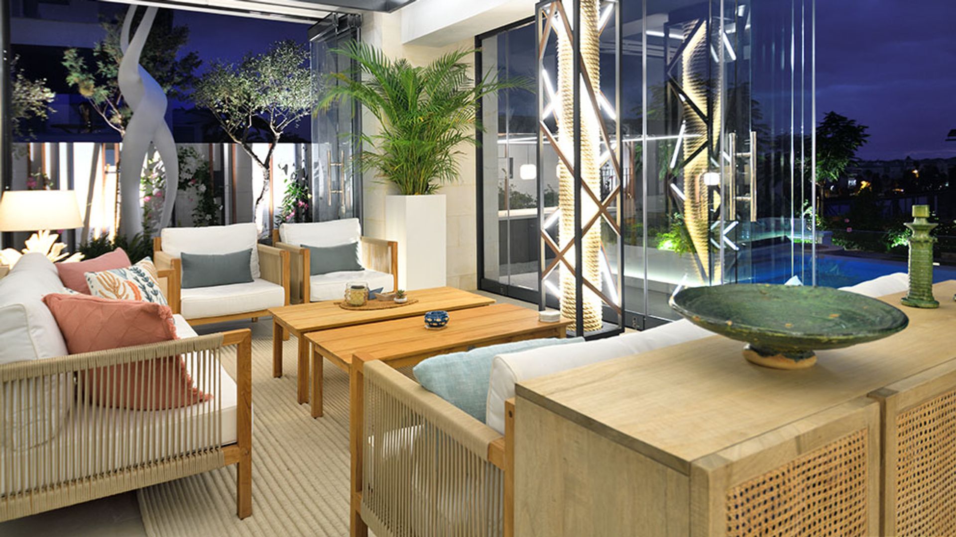 Espacio exterior de  noche a modo pabellón, con muebles de fibras vegetales, mesas de madera y plantas 