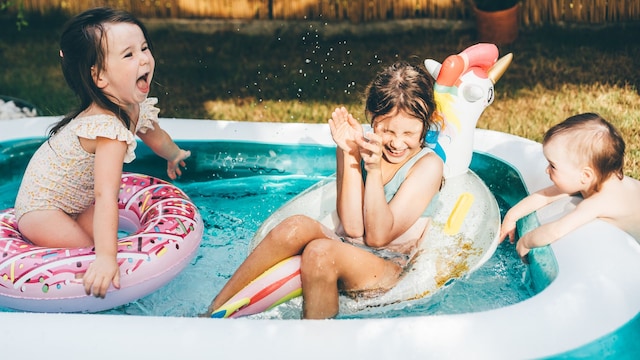 Niñas bañándose en la piscina hinchable en el jardín de su casa, con flotadores y salpicando agua.