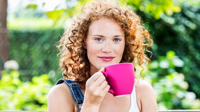 Mujer pelirroja y con el pelo rizado tomándose una infusión en una taza rosa