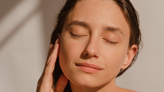 Mujer en primer plano sonriendo y tocándose el rostro con una mano, con los ojos cerrados, disfrutando de los rayos del sol