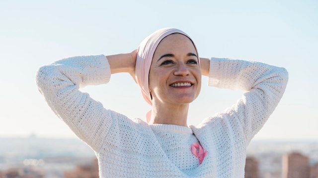 mujer sonriente con cáncer, con un pañuelo cubriéndole la cabeza y un lazo rosa